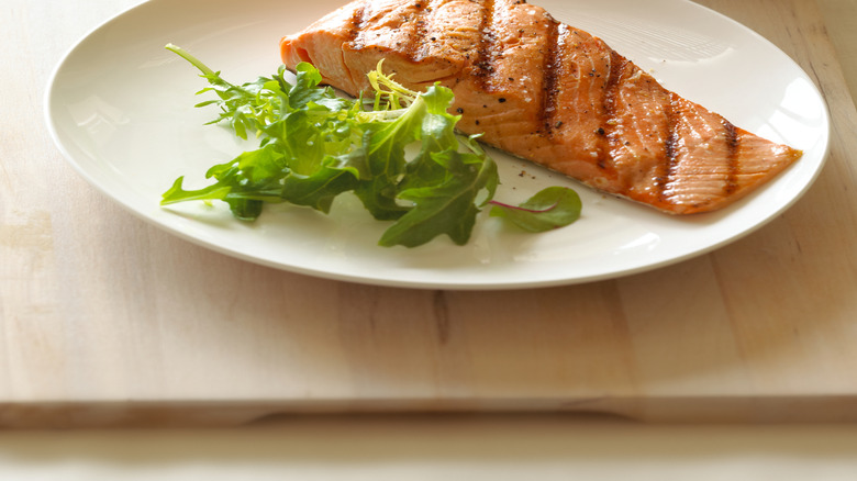 Grilled salmon on white plate with salad leaves