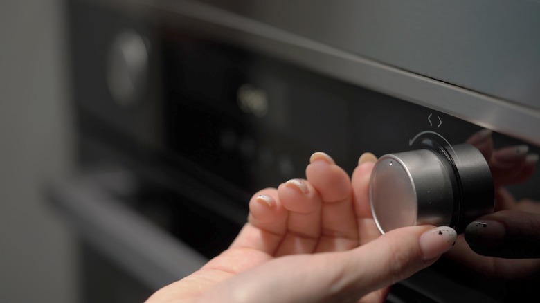 Woman's hand adjusting oven temperature