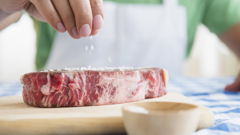 person putting salt on steak