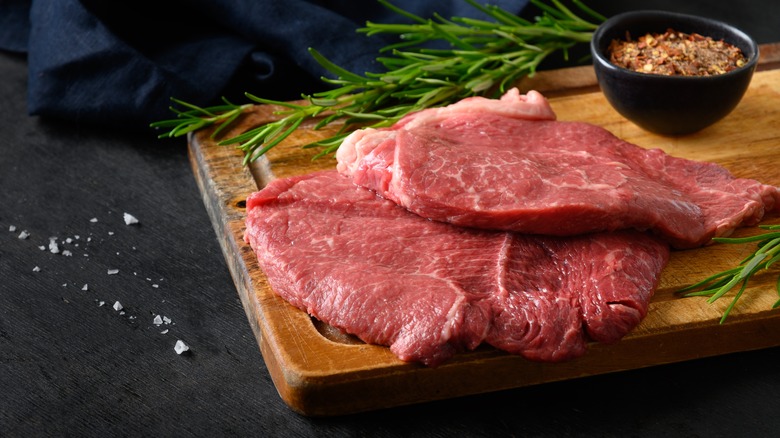 raw steaks on wooden board