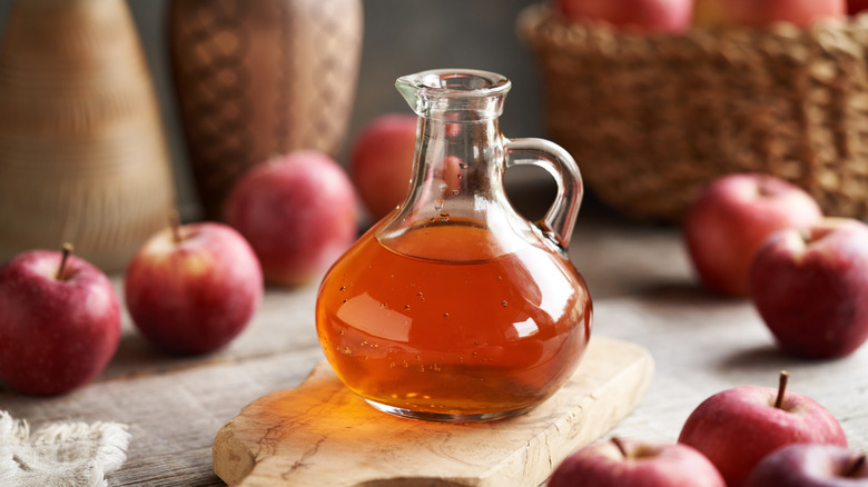 Glass jug of apple cider vinegar and red apples on table