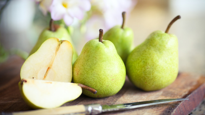 Cut and whole green pears on wooden board with knife