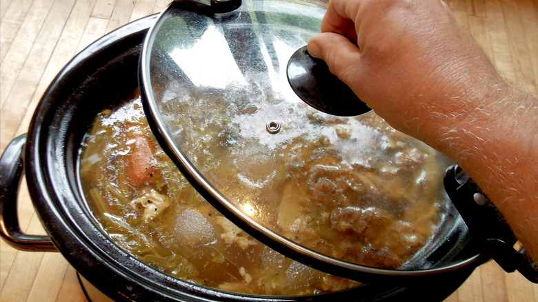 hand lifting lid on slow cooker