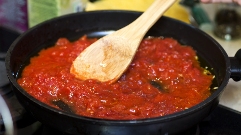 Pot of tomato sauce being stirred with a wooden spoon