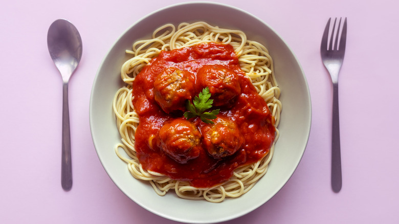 Spaghetti with meatballs and tomato sauce on a pink background