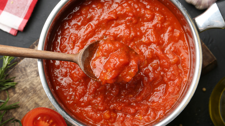 A spoon of chunky tomato sauce held over a full saucepan.