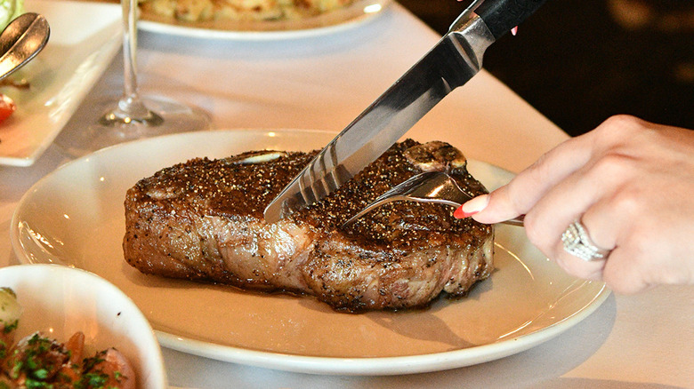 Hands cutting steak on plate