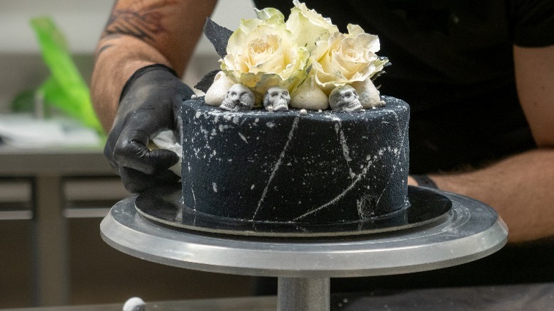 Black cake with white roses on cake turntable