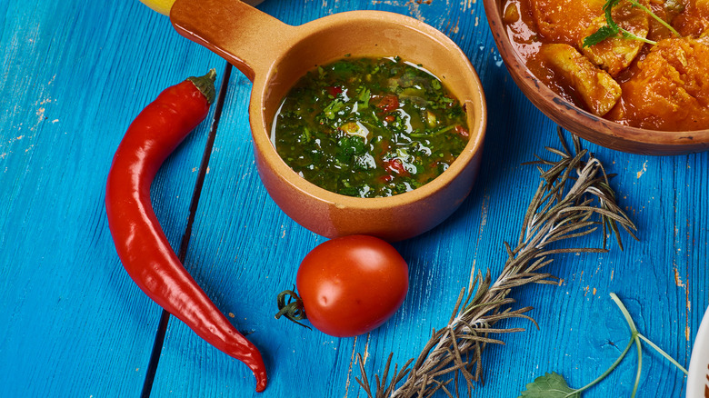 Earthenware bowl of chermoula sauce surrounded by chili, tomato, and herbs