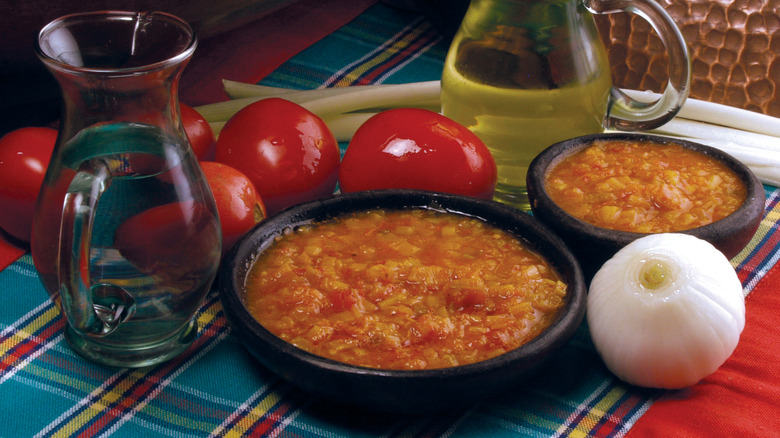 Two bowls of hogao sauce surrounded by tomatoes, an onion, and olive oil