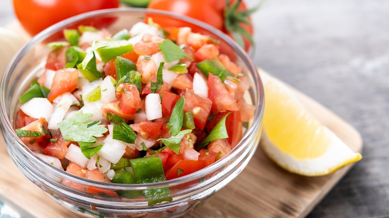 Glass bowl of pico de gallo with lemon wedge