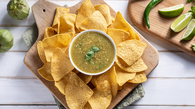 Bowl of salsa verde with chips on wooden cutting board