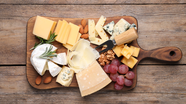 Cheeses and fruit on wooden board