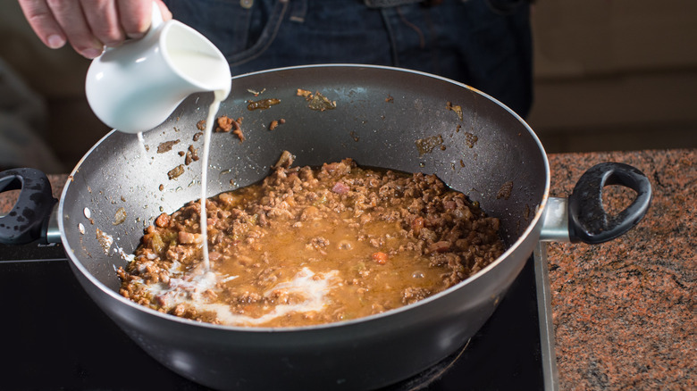 person adding milk to bolognese