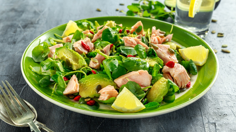 Salmon on greens with avocado and lemon wedges