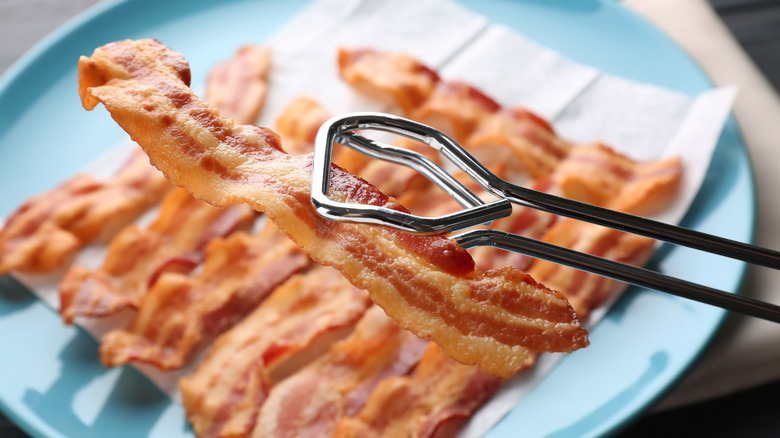 Tongs holding bacon piece