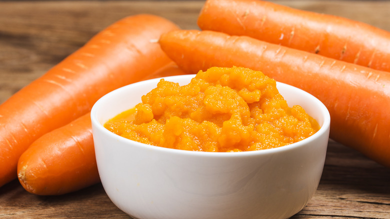 bowl of mashed carrots with whole carrots on side