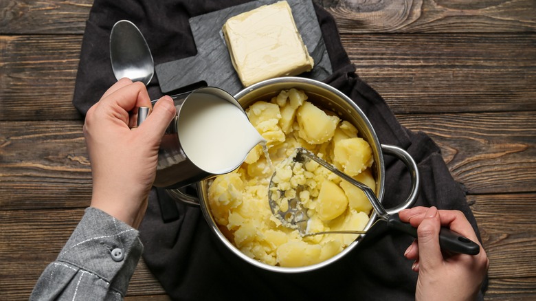 cook adding cream to pot of potatoes