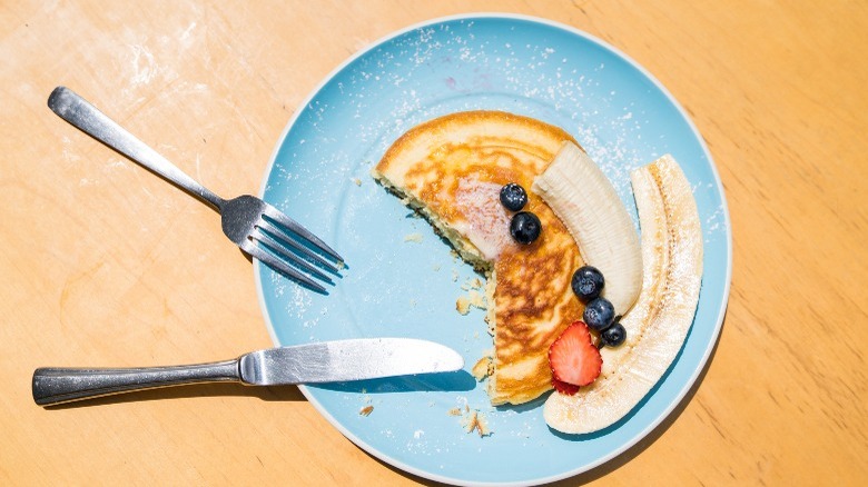 Half-eaten plate of pancakes and fruit