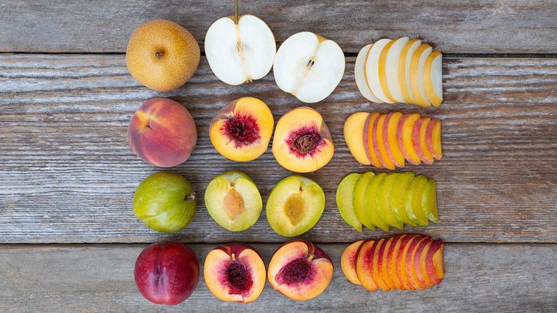 Whole, halved, and sliced pears, peaches, and plums on wooden board