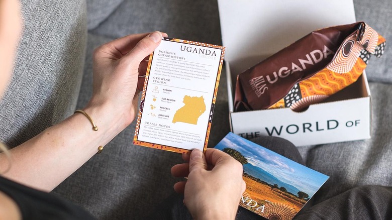 Person holding Uganda coffee card with Uganda coffee subscription box from Atlas Coffee Co