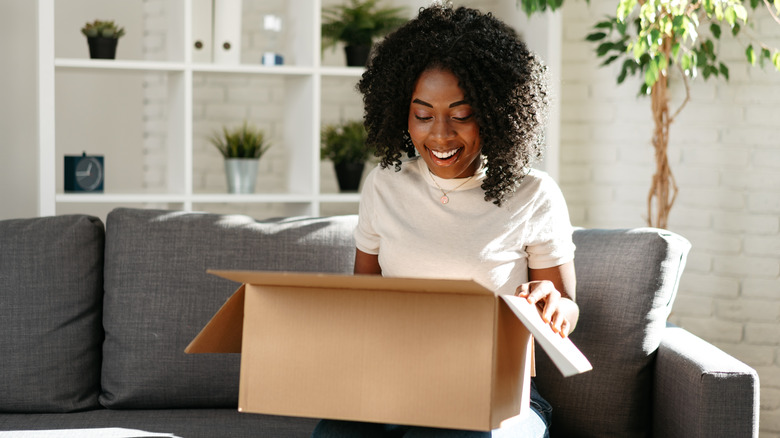 Woman smiling on couch opening cardboard box