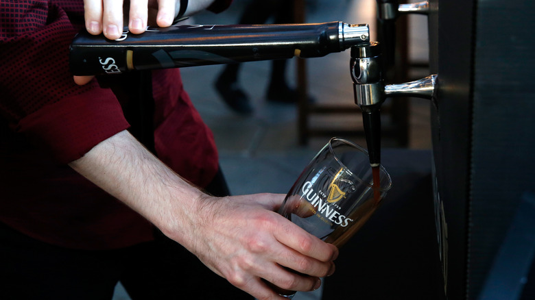 person pouring Guinness into glass