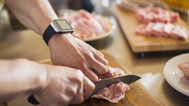 person cutting raw chicken on cutting board