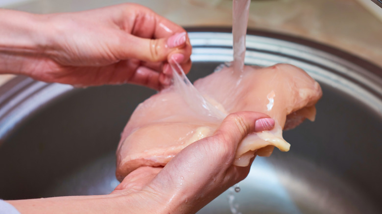 person washing raw chicken