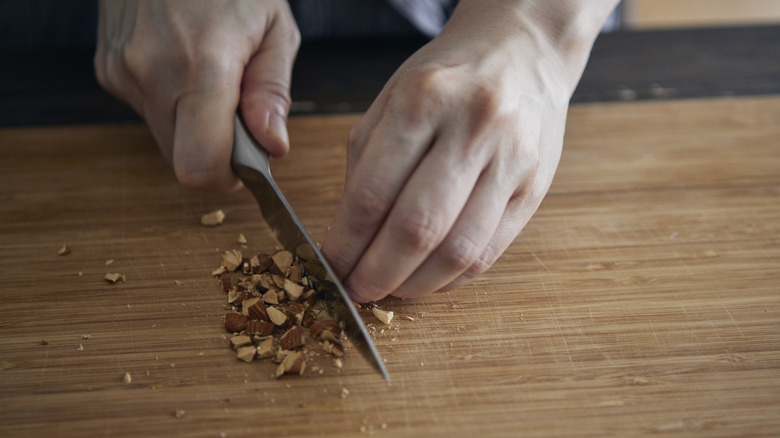 Hands chopping nuts on cutting board with knife