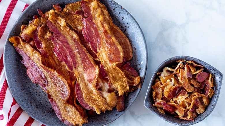 Crispy slices of bacon on a plate and bacon bits in a bowl