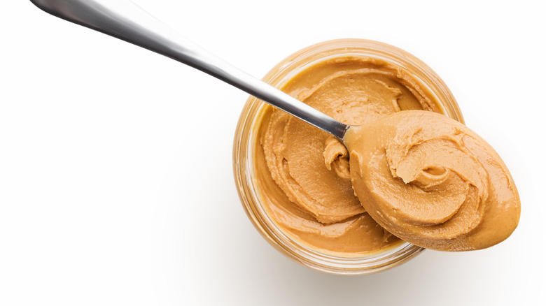 Peanut butter in glass jar with spoonful of peanut butter on top