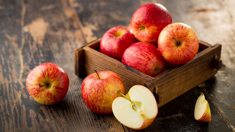 Wooden box of fresh whole apples with halved apple and sliced apple on wood counter