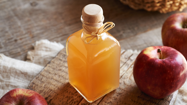 Jar of apple cider vinegar surrounded by fresh apples