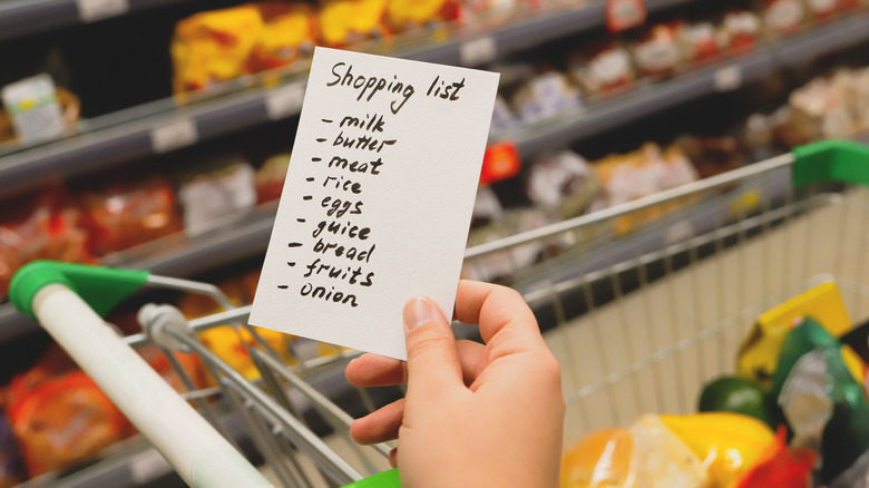 hand holding shopping list by cart