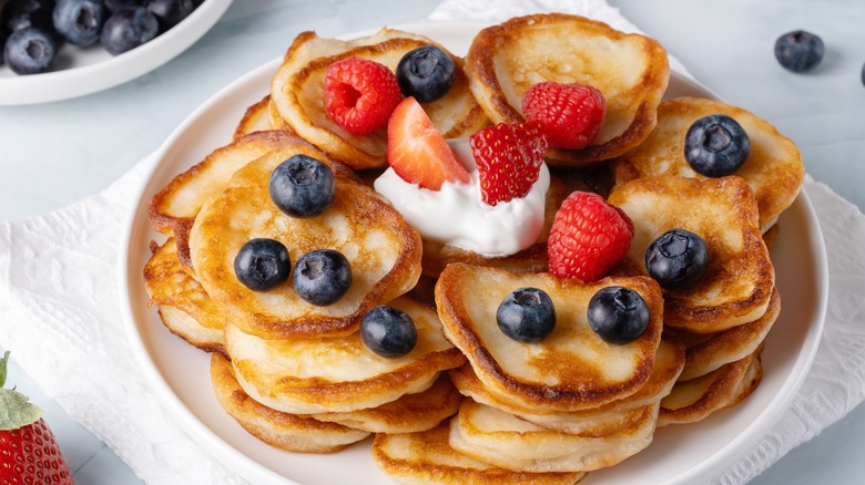 A plate full of mini pancakes topped with berries and cream