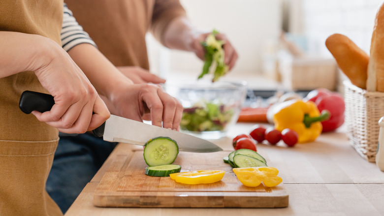 hands slicing vegetables on board