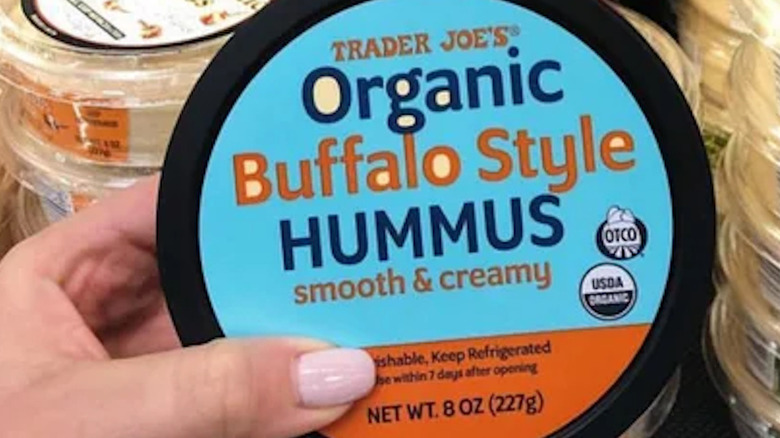 Hand holding TJ's Organic Buffalo Style Hummus in front of refrigerated display