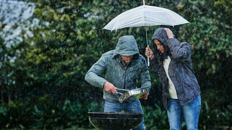 standing over grill with umbrella