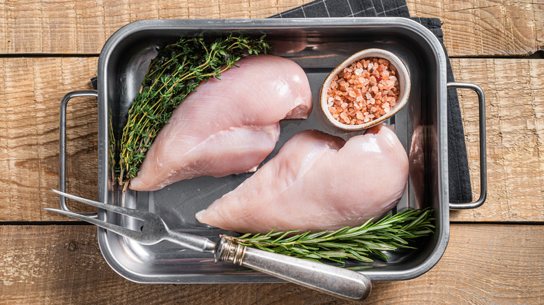 raw chicken breasts with rosemary, thyme, and salt ready to marinate