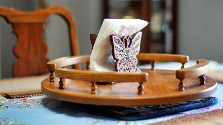 A wooden lazy Susan on a table with a butterfly napkin holder