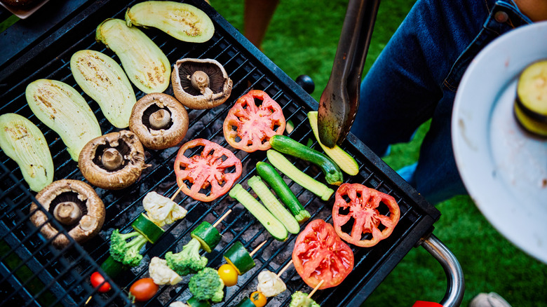 person using tongs on mixed veggies over grill