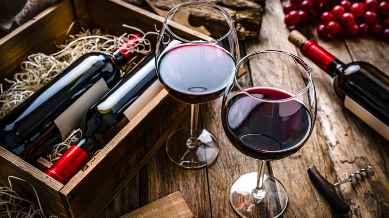 Vintage wines stored in a wooden case next to glasses of red wine