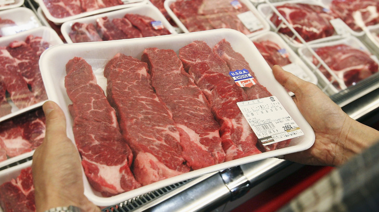 Hands holding package of pre-cut choice steak from Costco