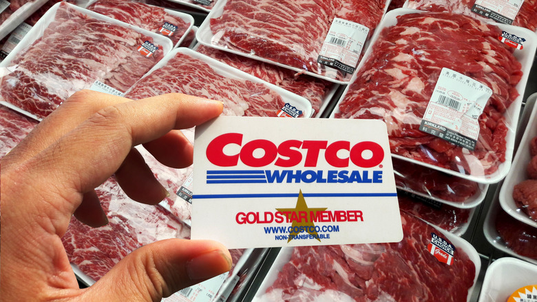 Hand holding Costco membership card in front of case of cuts of beef