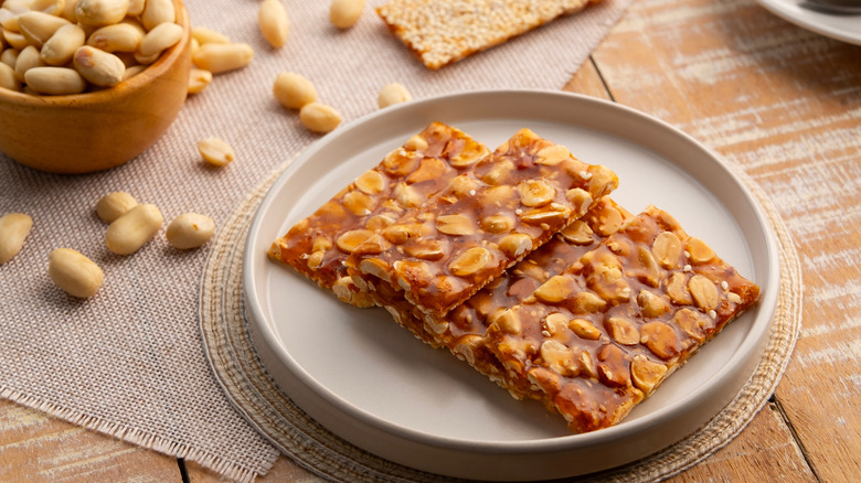 peanut brittle with sesame on a white plate next to a bowl of peanuts