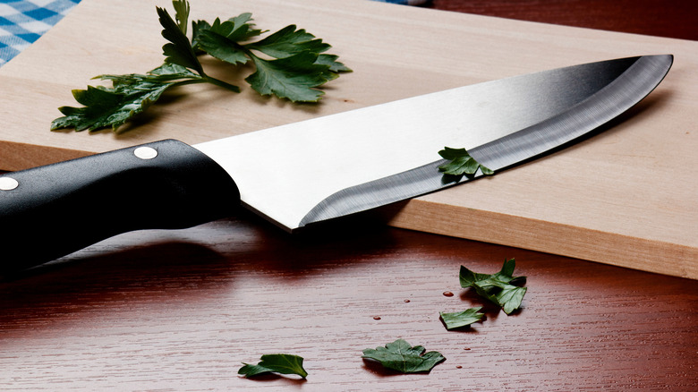 kitchen knife with herbs on cutting board