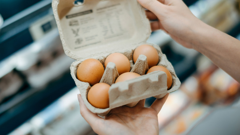 hands holding open carton of eggs in grocery store