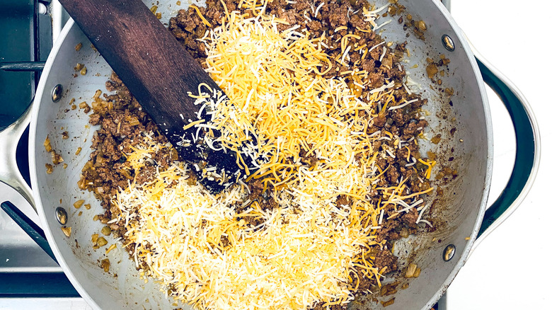 shredded cheese over ground beef in pan