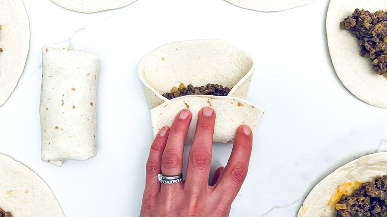 Hand with rings rolling up chimichangas